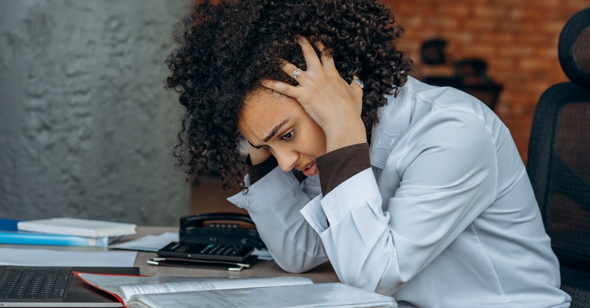 Woman sitting at desk appearing stressed while reviewing documents in an office setting.